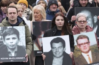 Personnes prenant part à une marche pour commémorer le 50e anniversaire du Bloody Sunday à Derry, portant des images des victimes.